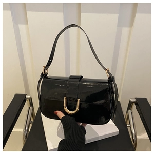 Detail shot of glossy black patent leather shoulder bag featuring a gold horseshoe buckle