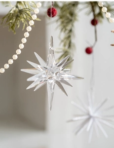 Close-up of clear multi-faceted star ornament hanging on a festive Christmas tree branch