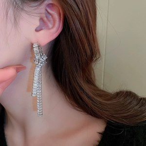 Silver bow earrings with tassels and zircon inlay shown on model in a close-up shot
