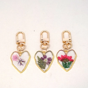 Three heart-shaped resin keychains with colorful real dried flowers and gold metal frames