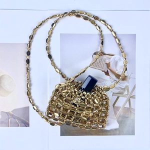 Detailed shot of a gold bead woven micro handbag with lipstick for scale and a long chain