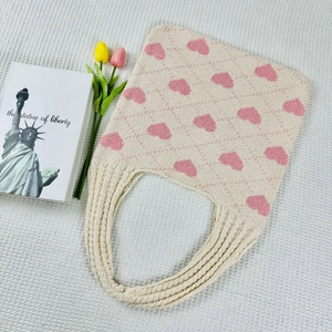Detail view of beige knit tote bag with pink heart pattern on white textured background