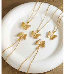 Detailed view of gold butterfly necklaces with cubic zirconia on a white ceramic plate