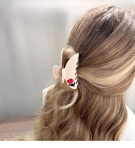 Close-up of a cream hair claw clip with red floral motifs on long wavy brown hair