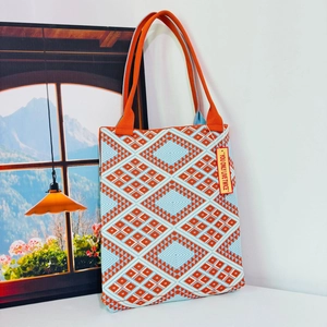 Detail of geometric knit tote bag with orange and blue diamond pattern and slogan tag