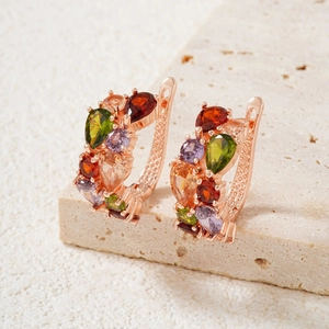 Rose gold huggie earrings with colorful pear-cut zircon stones on a stone surface