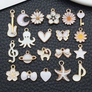 Flat lay of 20 white and gold enamel charms in shapes like hearts, stars, and musical notes