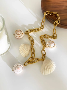 Detail of chunky gold chain necklace featuring seashell and conch charms on white surface