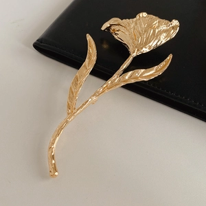 Detail of a gold metallic flower brooch with hammered texture on black leather