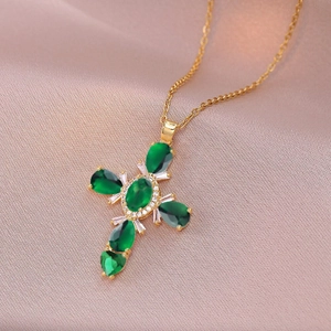 Close-up of gold-plated cross necklace with green and clear zircon stones on pink fabric