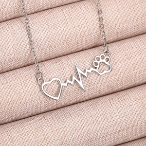 Close-up of a silver heart necklace with a pet paw and heartbeat line on pink fabric