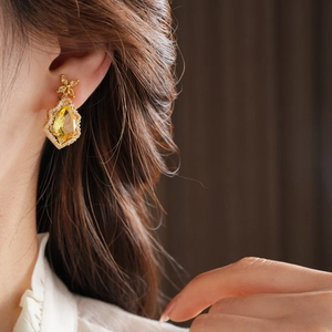 Detail of luxury gold rhombic drop earrings with yellow gemstone on female model