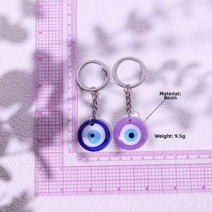 Detail view of Evil Eye resin keychains in blue and purple on a pink grid background