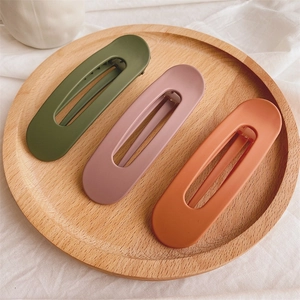 Three large matte duckbill hair clips in dark green, dusty pink, and caramel displayed on wood