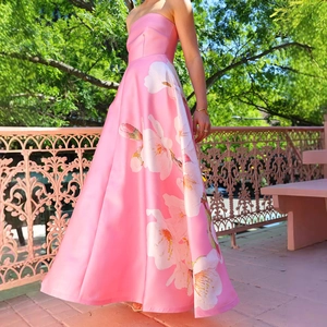 Detail eines rosa Satin-Maxikleids mit weißem Blumendruck in einer Gartenumgebung
