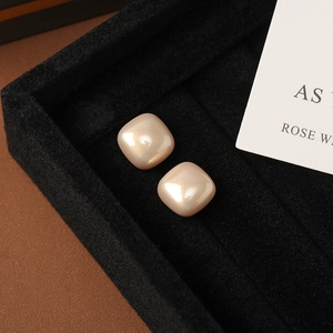 Macro shot of geometric square pearl earrings resting on premium black velvet jewelry box