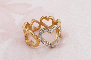 Close-up of golden hollow heart ring featuring sparkling pavé diamonds on a pink background