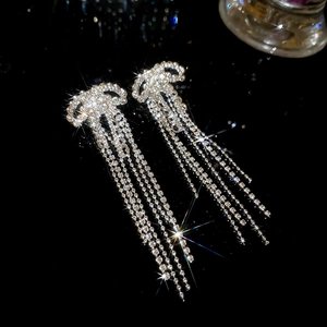 Detailed view of silver bow earrings with sparkling rhinestone tassels on dark background