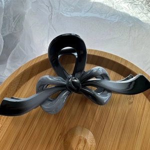 Detail view of large resin bow hair claw with black-grey gradient on a wooden plate