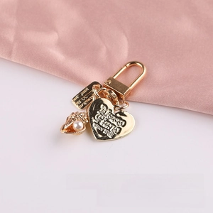 Detail of golden keychain with pearl shell and embossed heart charm on pink silk