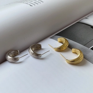 Detailed view of silver and gold C-shape stud earrings with vertical wavy texture
