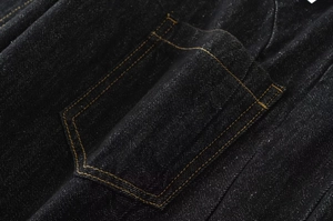 Dettaglio macro di denim nero con cuciture arancioni a contrasto sulla tasca posteriore
