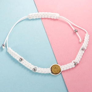 Macro shot of white woven bracelet featuring silver beads and a golden Saint Benedict medal