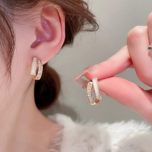 Detailed view of C-shaped gold-plated earrings with zircon and shell inlay details