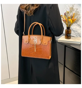 Brown crocodile texture handbag detail featuring a metallic S-logo and fringe tassel