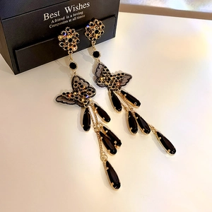 Detail of black butterfly tassel earrings with rhinestones and lace on a white surface
