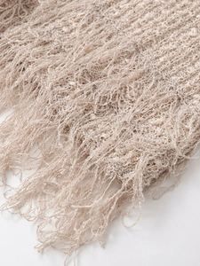 Detailaufnahme des beigen Strickgewebes mit weichen Quastenrändern am Saum