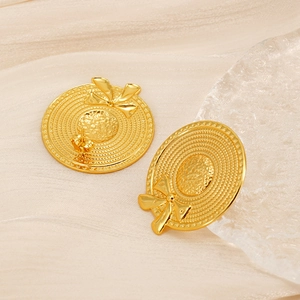 Macro shot of gold sun hat stud earrings with bow detail on white satin background
