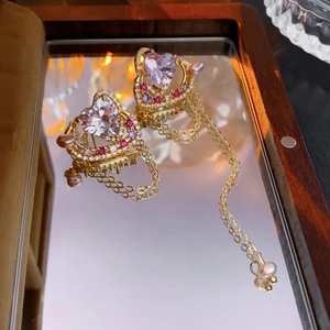 Détail de boucles d'oreilles cœur en cristal rose avec pompons dorés et perles