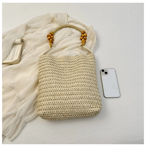 Detail of beige straw handbag featuring a decorative wooden bead handle and woven texture