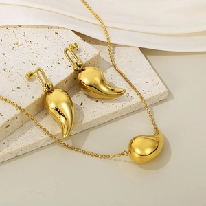 Ensemble collier et boucles d'oreilles goutte dorés sur un support en travertin
