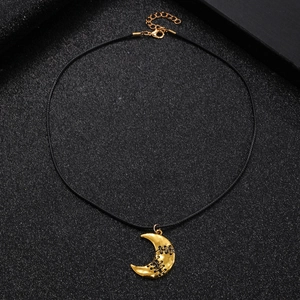 Macro view of golden crescent moon pendant with black stitched detail on black background