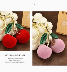 Detail of red and purple flocked cherry keychains with gold metal and green leaves