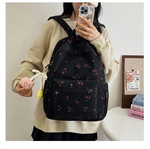 Back view of a black corduroy backpack featuring red cherry prints and flower charm