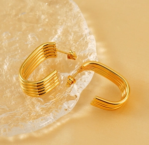 Macro detail of layered gold-plated C-shaped earrings on smooth yellow silk fabric