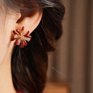 Detail view of model wearing red enamel flower earrings with zircon and gold plating