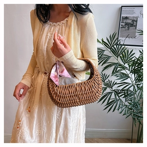 Detail of a brown crescent-shaped rattan tote bag decorated with a stylish pink silk scarf