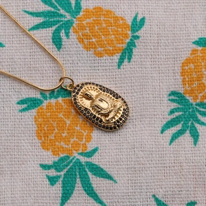 Golden snake chain necklace featuring an oval Buddha pendant with black zircon stones