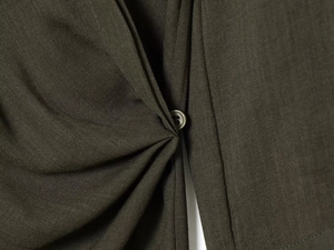 Macro shot of dark olive woven fabric texture and button detail on asymmetric top