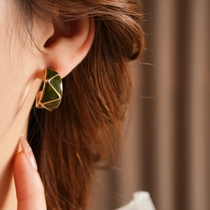 Close-up of vintage gold C-shape earrings with green enamel geometric texture on model