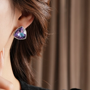 Gros plan d'une boucle d'oreille triangle en pierre violette sur l'oreille d'un mannequin