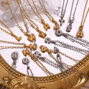 18K gold and silver plated bubble letter necklaces displayed on a mirrored water surface