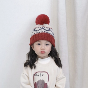Detail of red and beige knit kids' beanie with blue geometric patterns and soft pom-pom