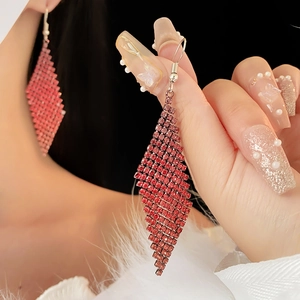 Détail de longues boucles d'oreilles à pompons avec strass rouges et forme de losange