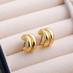 Macro detail of gold-plated striped C-shaped earrings on a beige velvet jewelry display