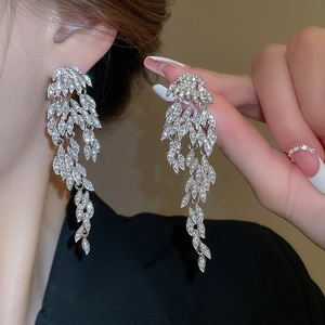 Close-up of sparkling silver leaf tassel earrings with rhinestones on a female model